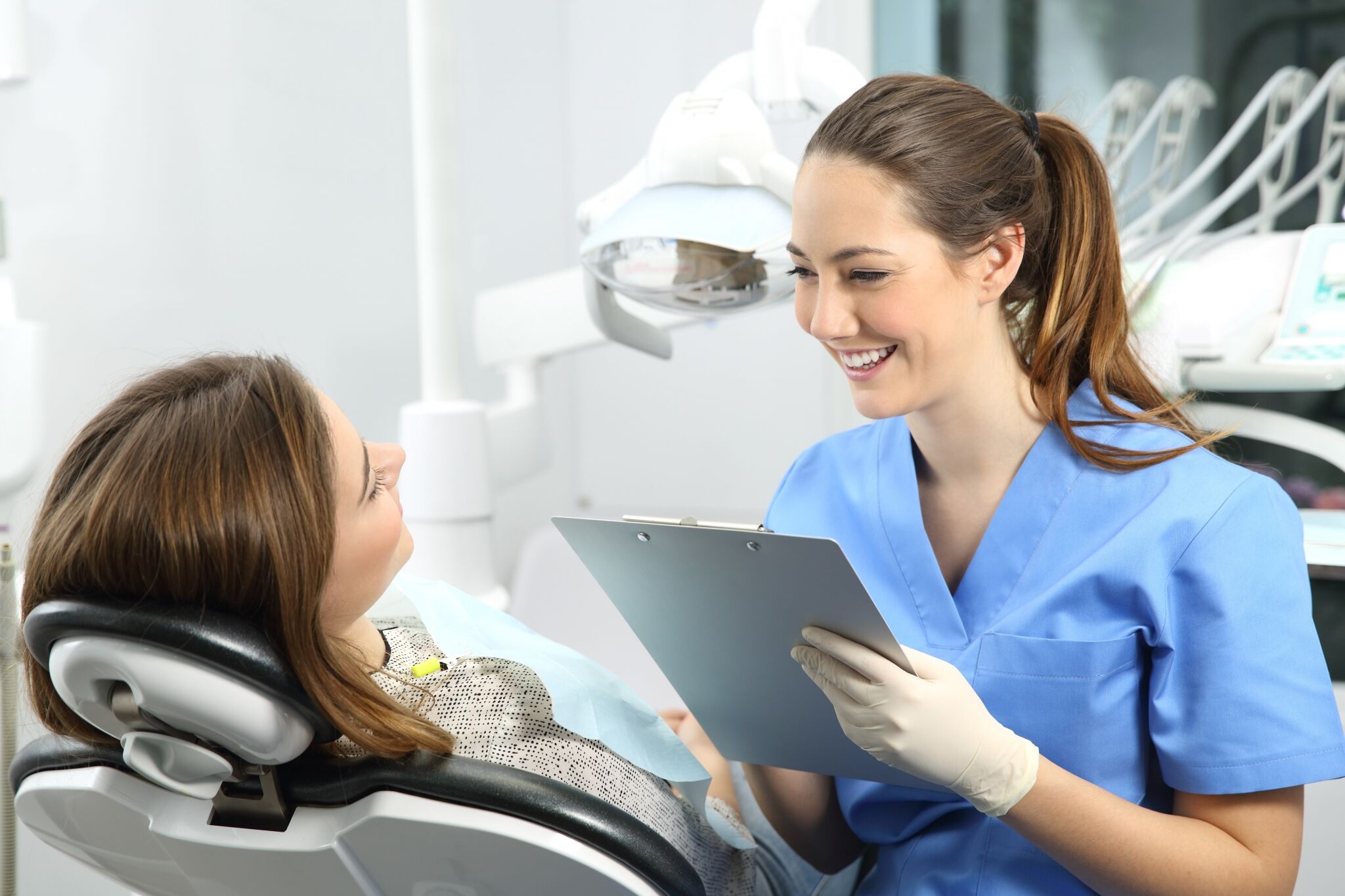 Dental student in blue scrubs working with a patient and filling out paper work