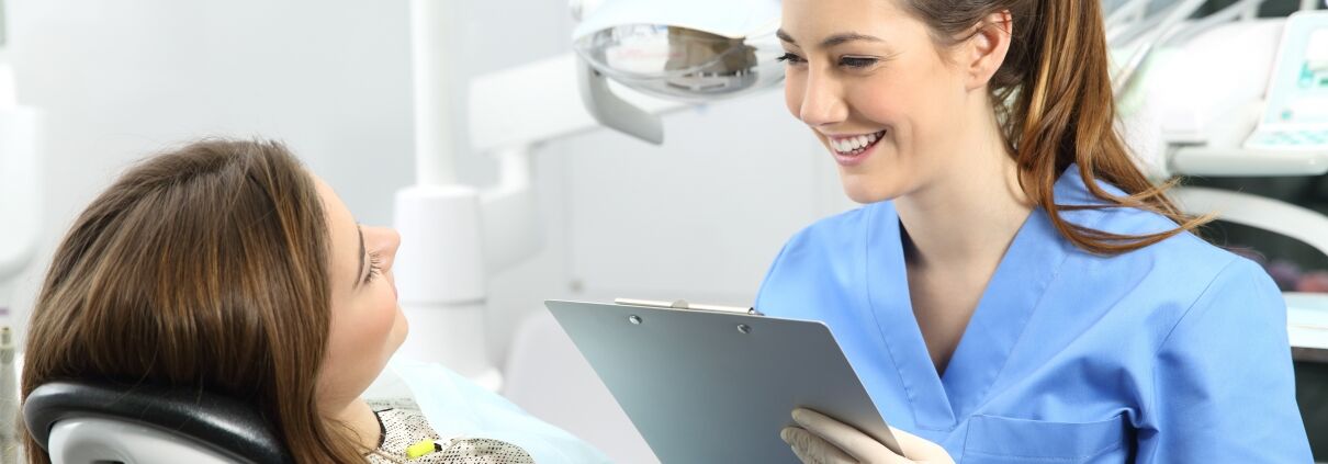 Dental student in blue scrubs working with a patient and filling out paper work